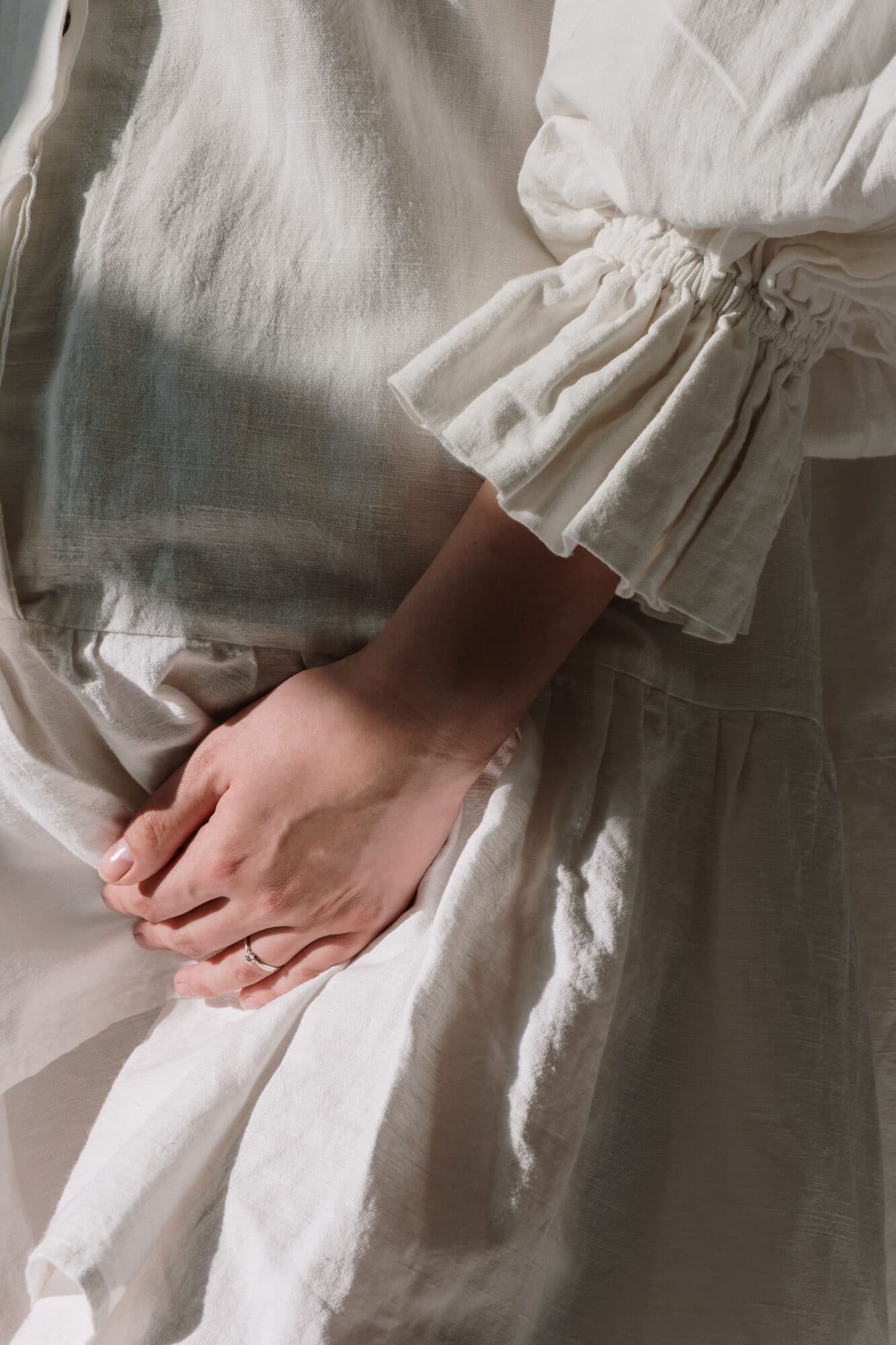 Hands resting together in a lap, in soft white linen