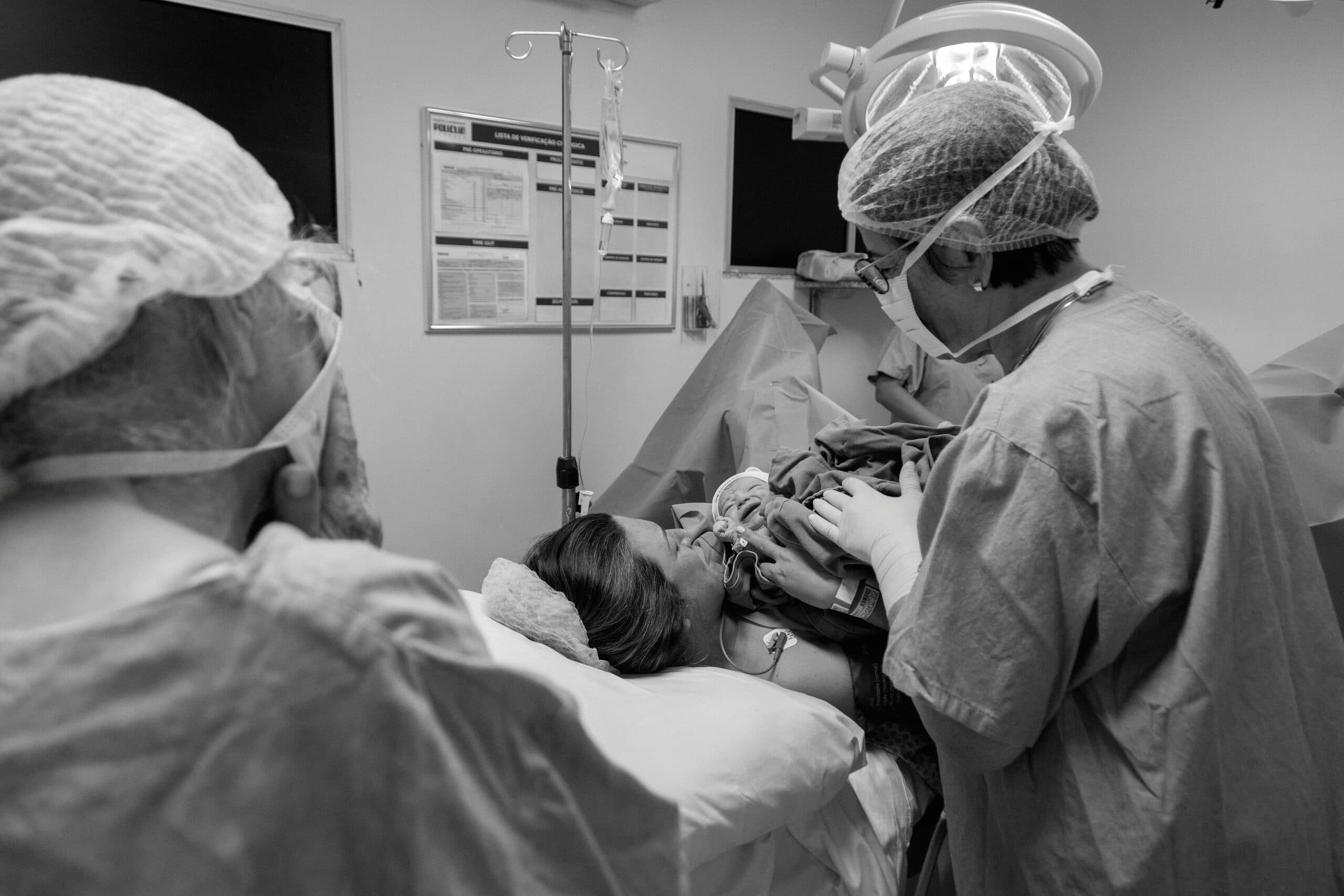 A mother in theatre meeting her newborn just after a caesarean, the team in caps and masks around her