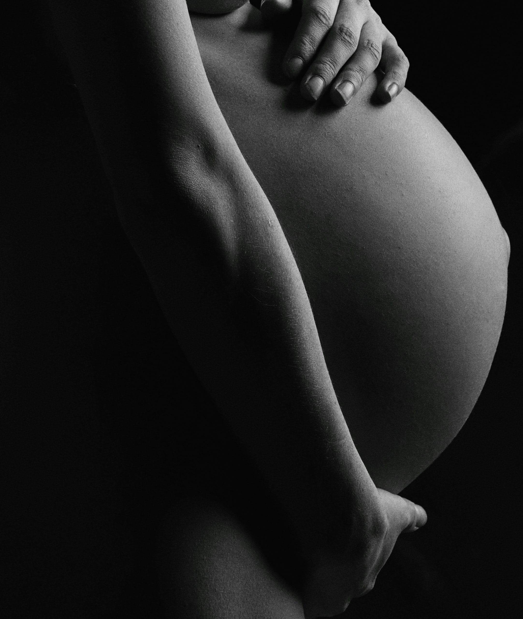 A hand resting on a pregnant belly, lit against a dark ground