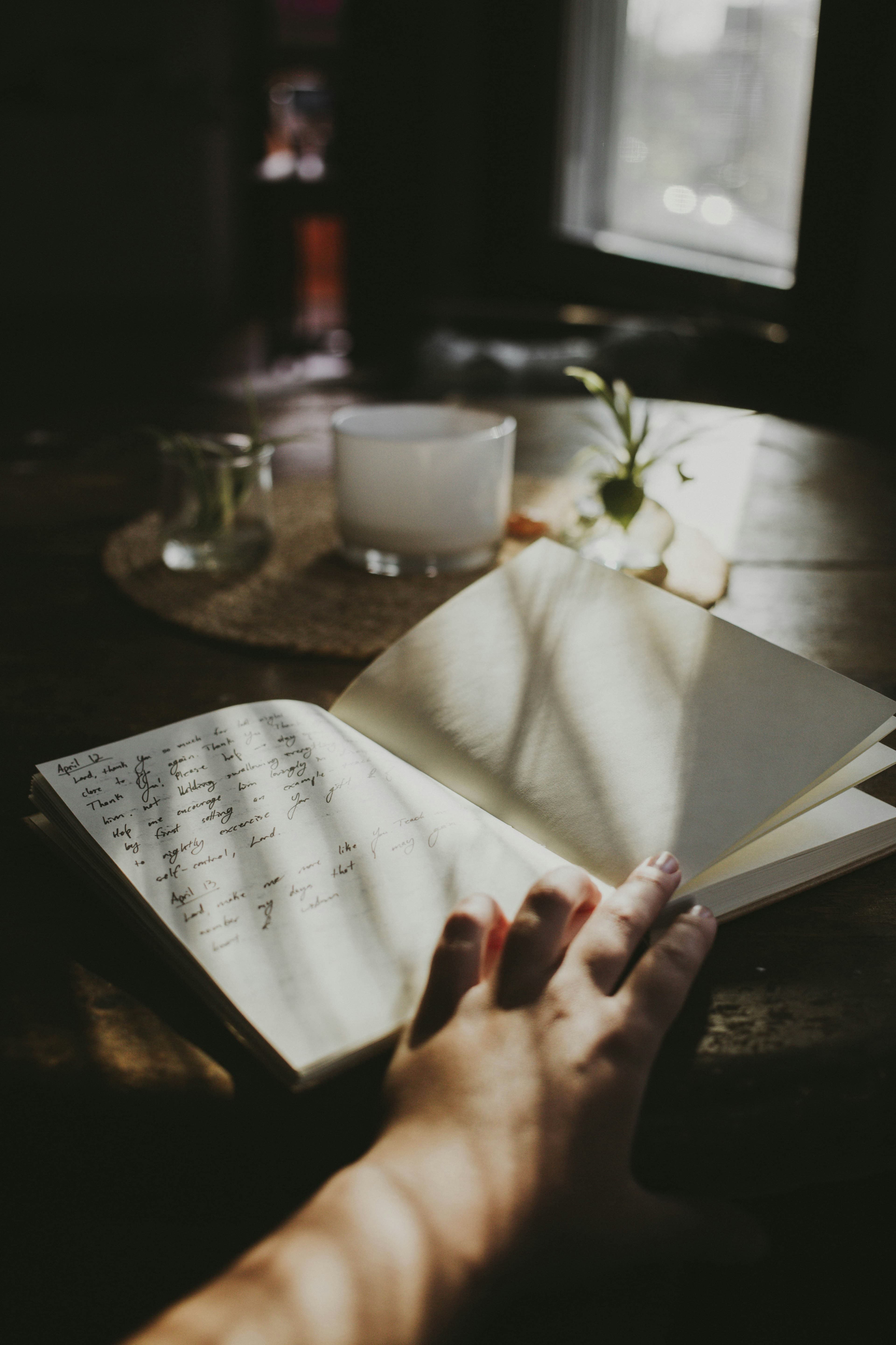 A hand turning the pages of a handwritten journal in soft window light, beside a candle